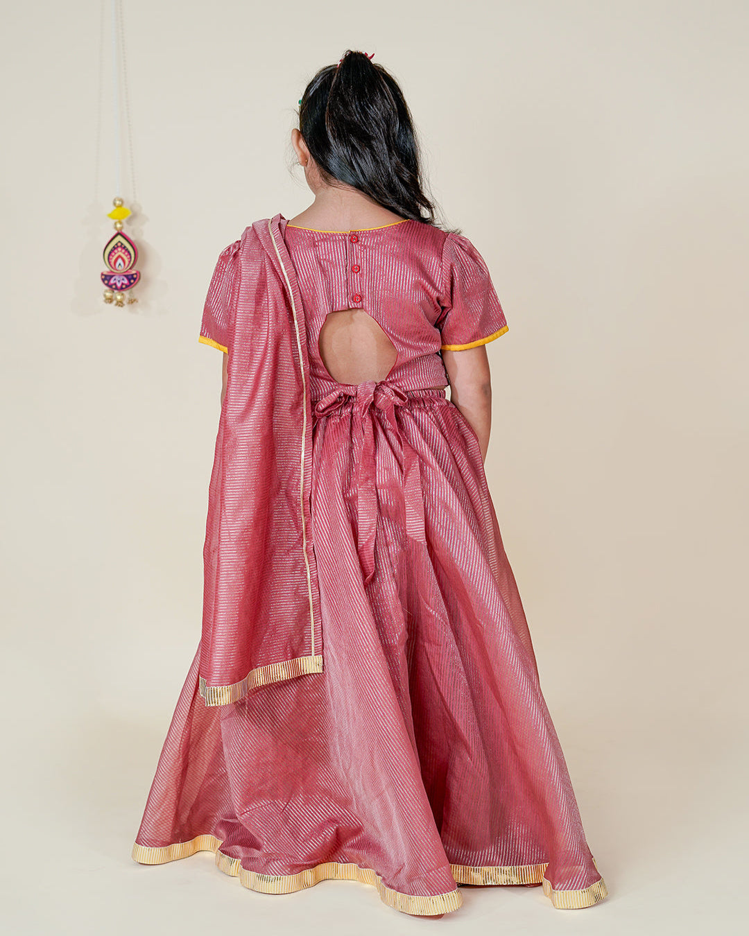 Person wearing a pink traditional outfit with a cut-out design on a beige background