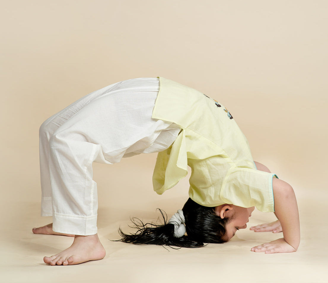 Girl performing Chakrasana yoga pose wearing Chanda Mama Krishna Surya Namaskar kids yoga set – pista green top with hand block print and white cotton pants.