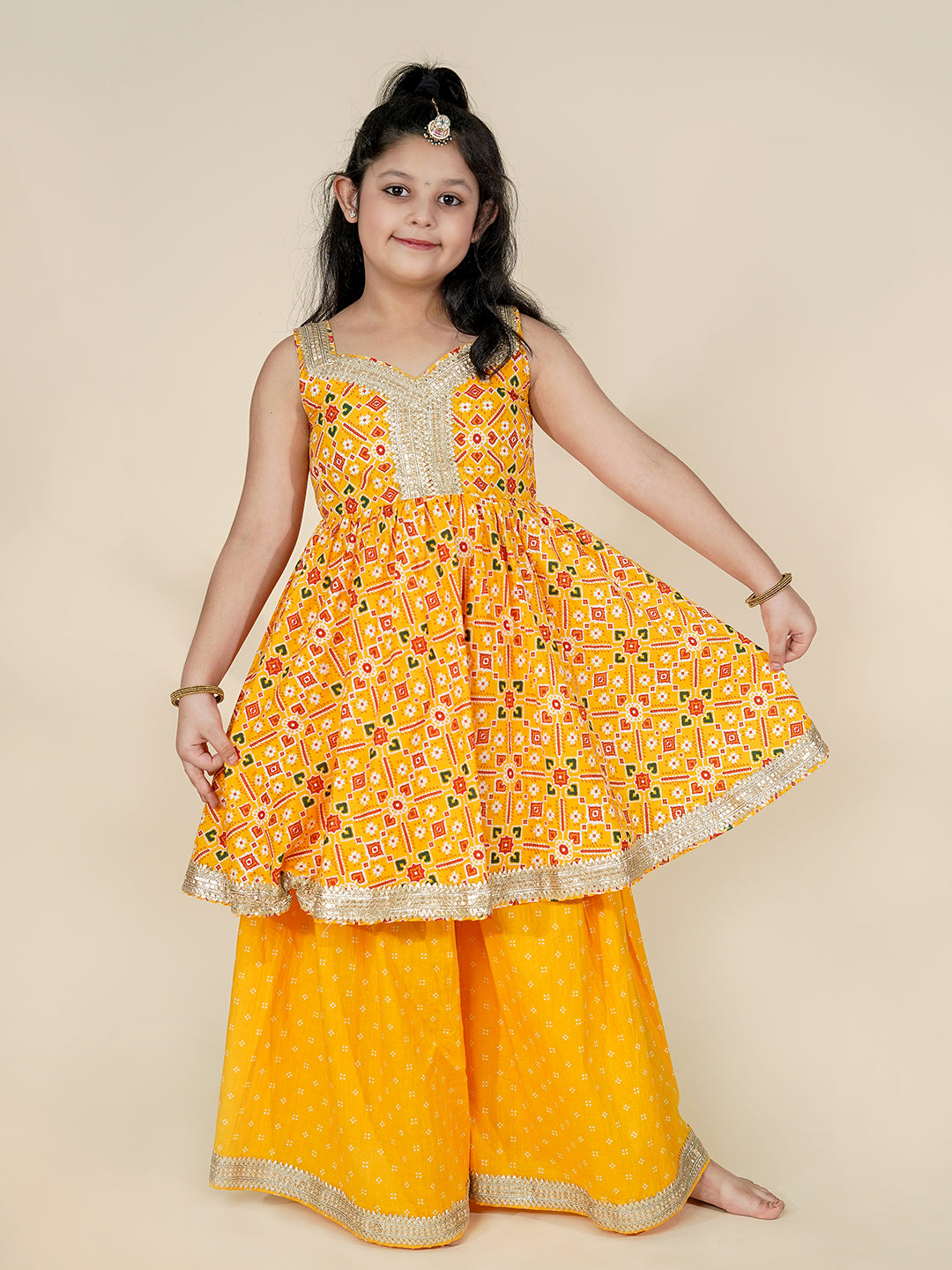 Young girl wearing a yellow traditional outfit with a patterned top and palazzo pants on a beige background