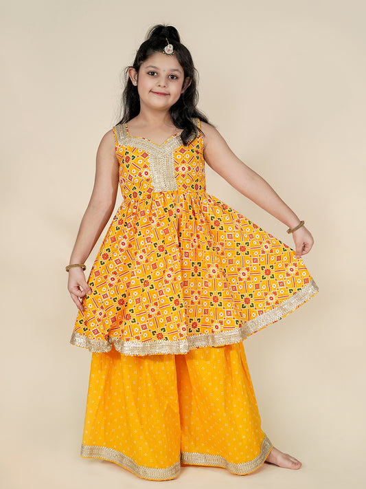 Young girl wearing a yellow traditional outfit with a patterned top and palazzo pants on a beige background