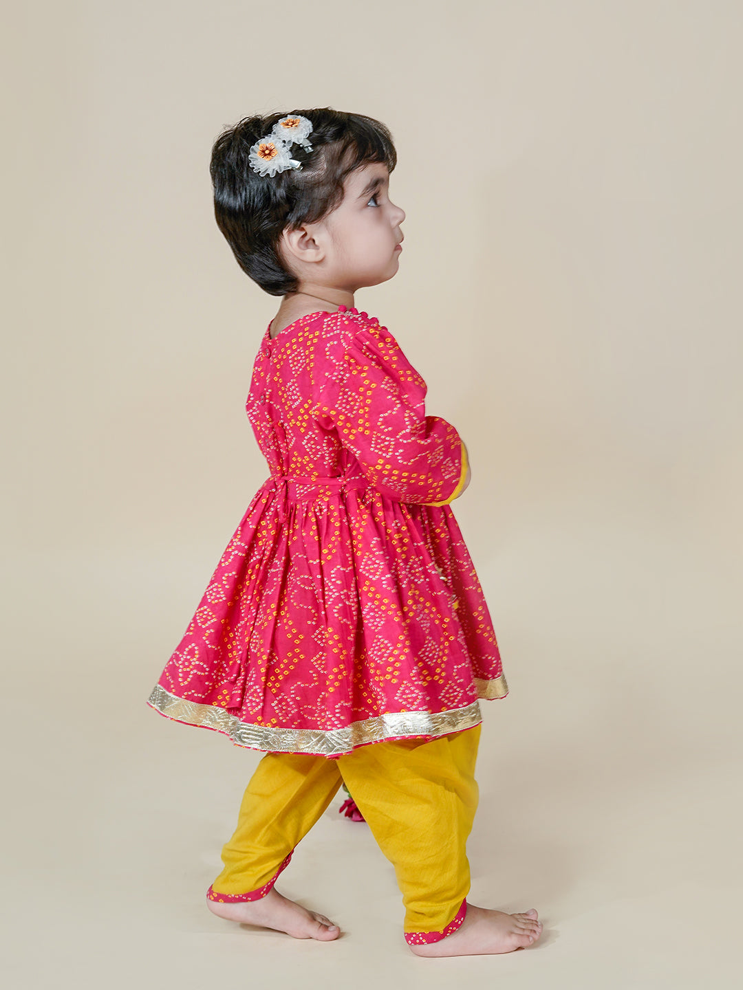Child wearing a pink and yellow traditional outfit on a beige background