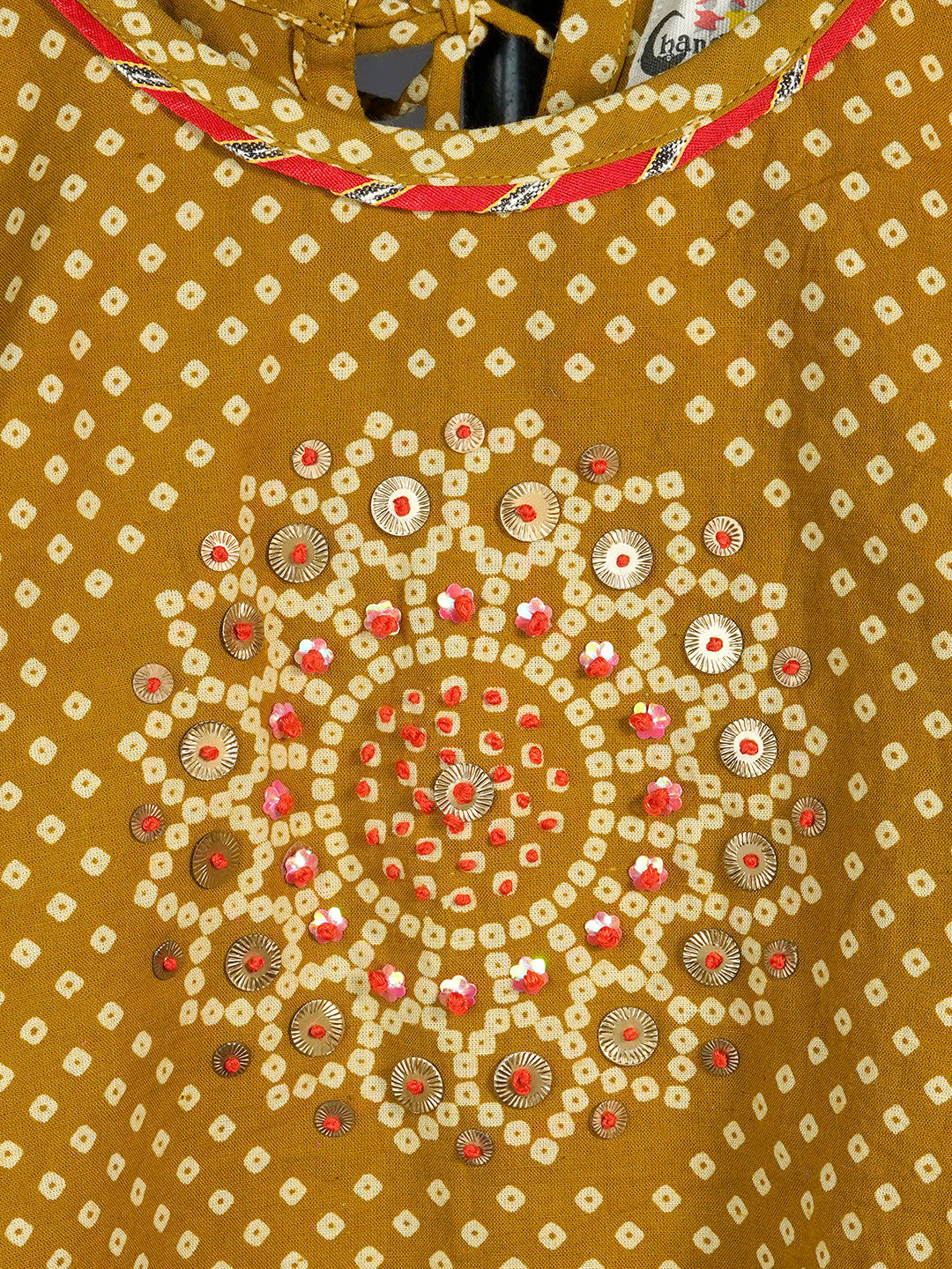 Close-up of a mustard yellow garment with intricate white and red patterns.